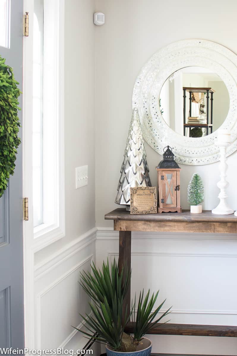 The corner of the front door with a edge of a green wreath, and to the right, a console table with holiday decor