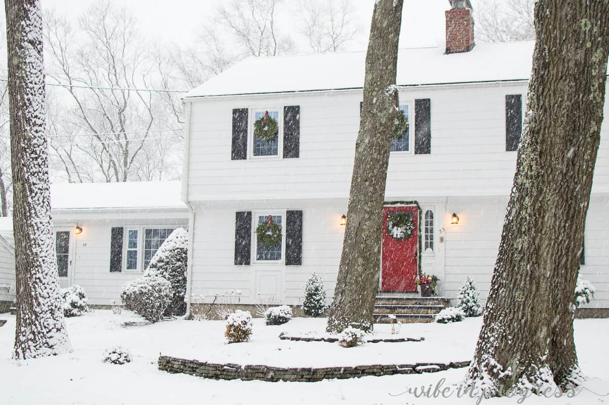 A two-story home with white siding and a red door, on a snowy day