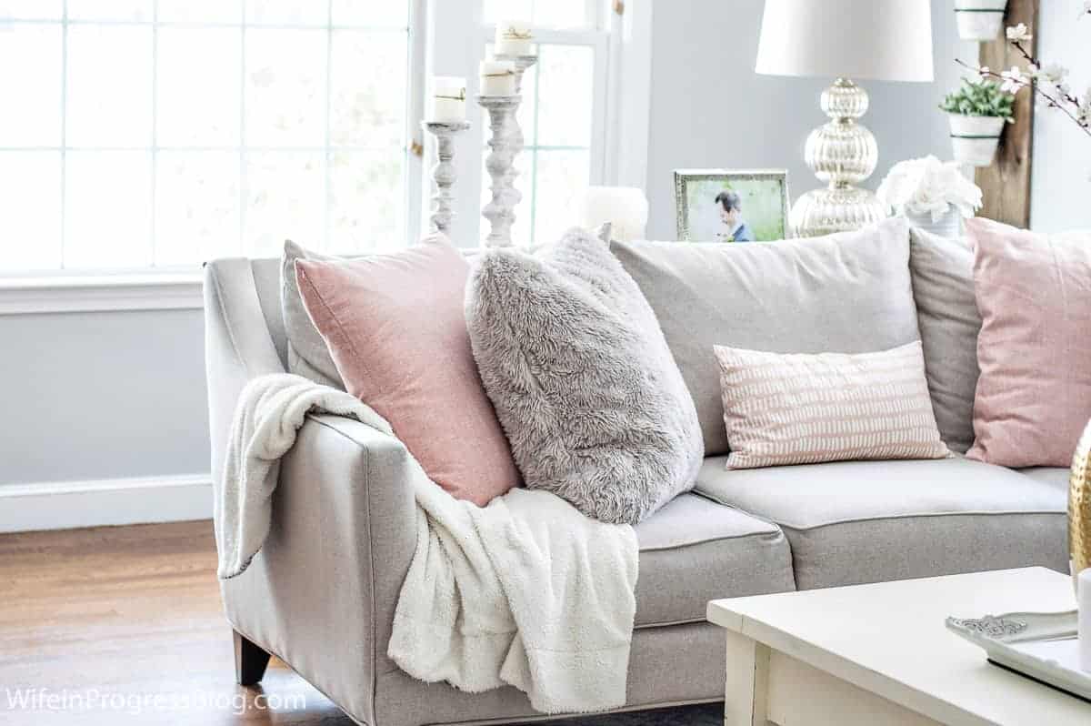 Large pink and grey pillows on a light grey sofa, with an off-white coffee table in front 
