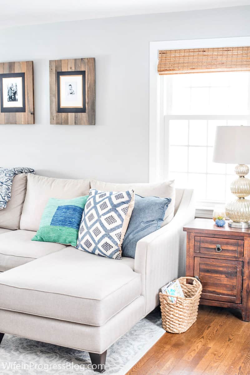 Blue and green pillows on a light grey sofa, and a small blue potted plant on a wooden side table