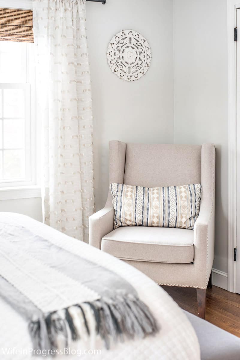 A neutral chair arrange in the corner of this small master bedroom adds functionality to the space