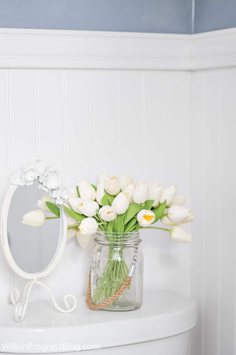 A closer look at bathroom accessories - white mirror and large mason jar with rope handle, holding white tulips