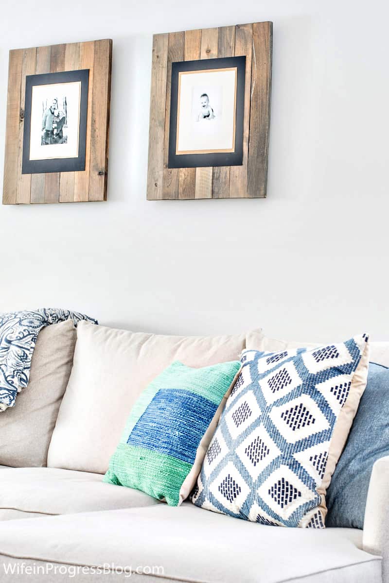 Blue, white and green throw pillows on a sofa, with family portraits in rustic wood frames above