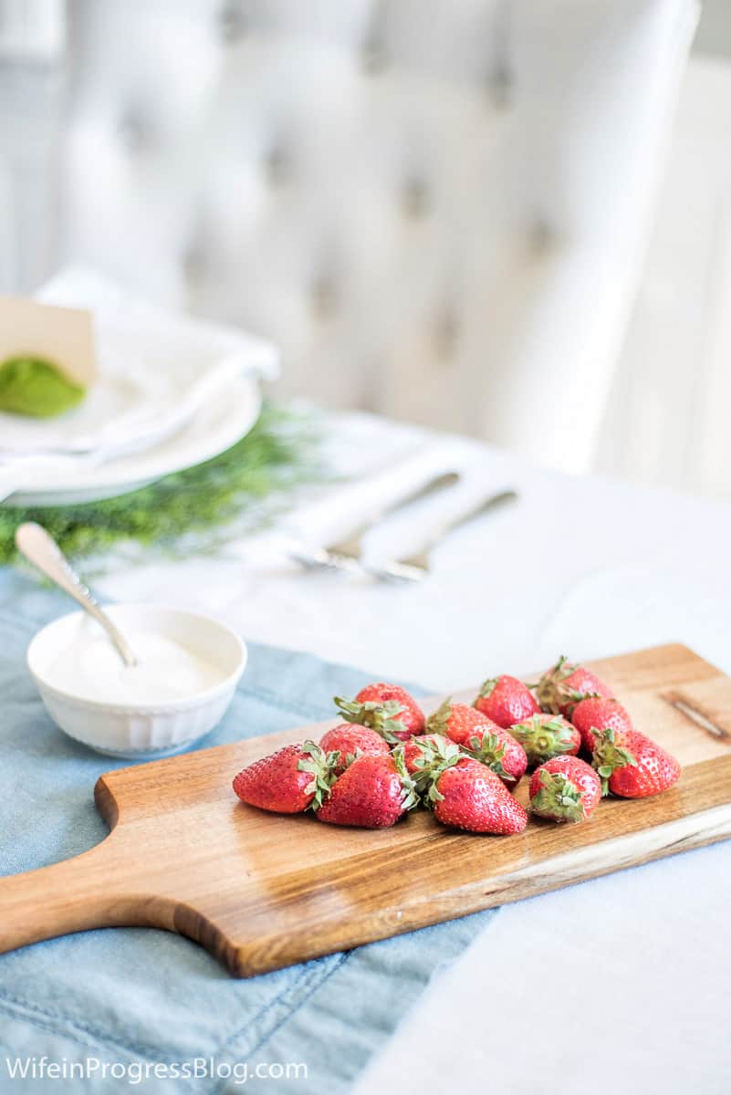 A dozen strawberries resting on a wooden board near the place settings