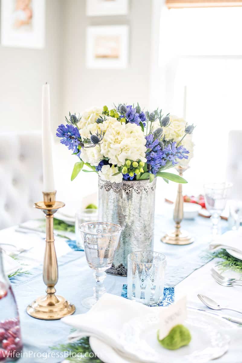 A metal vase of flowers, white tapered candles in gold candle holders, and stemware with gold detailing