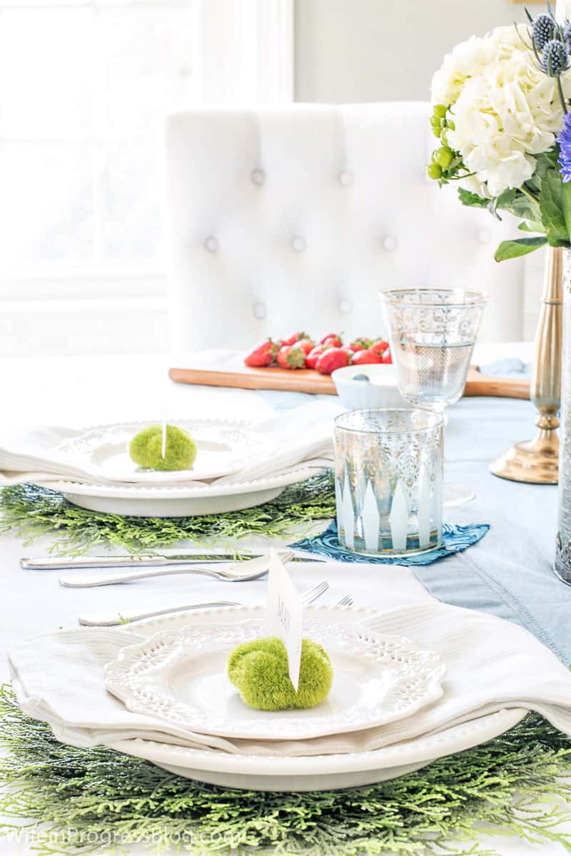 Tumblers with gold detail, resting on patches of blue fabric, near place settings on a light blue table runner