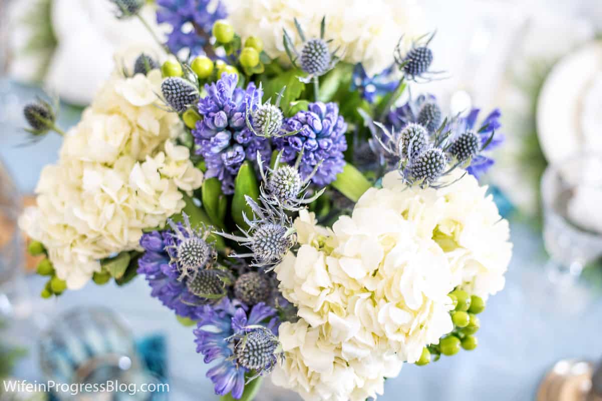 A close up of the floral centerpiece with blue and white flowers and greenery