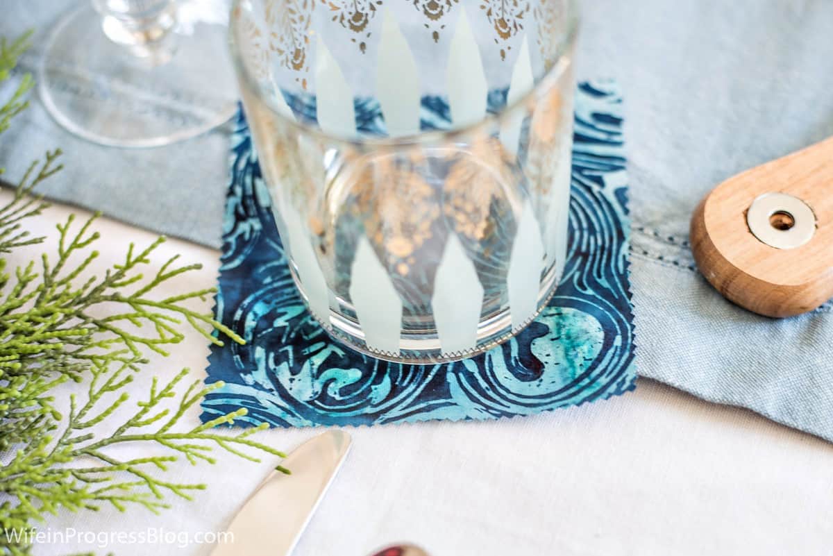 A clear tumbler with gold detailing on a swirly blue napkin
