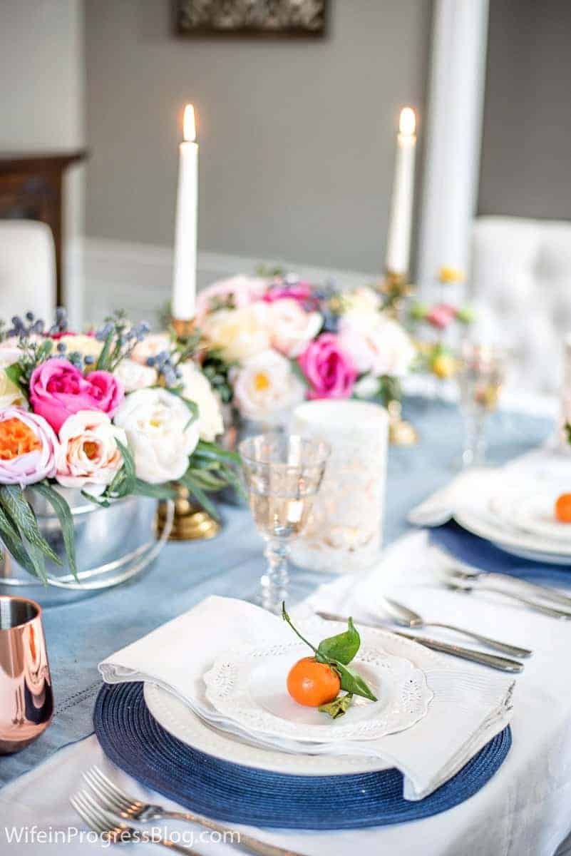 Simple and elegant Mother's Day tablesetting with flower arrangement, stemmed oranges, and blues and whites