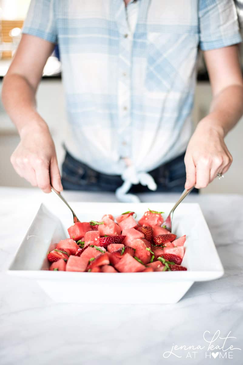 Woman mixing a refreshing watermelon, basil, and strawberry salad for a summer paty