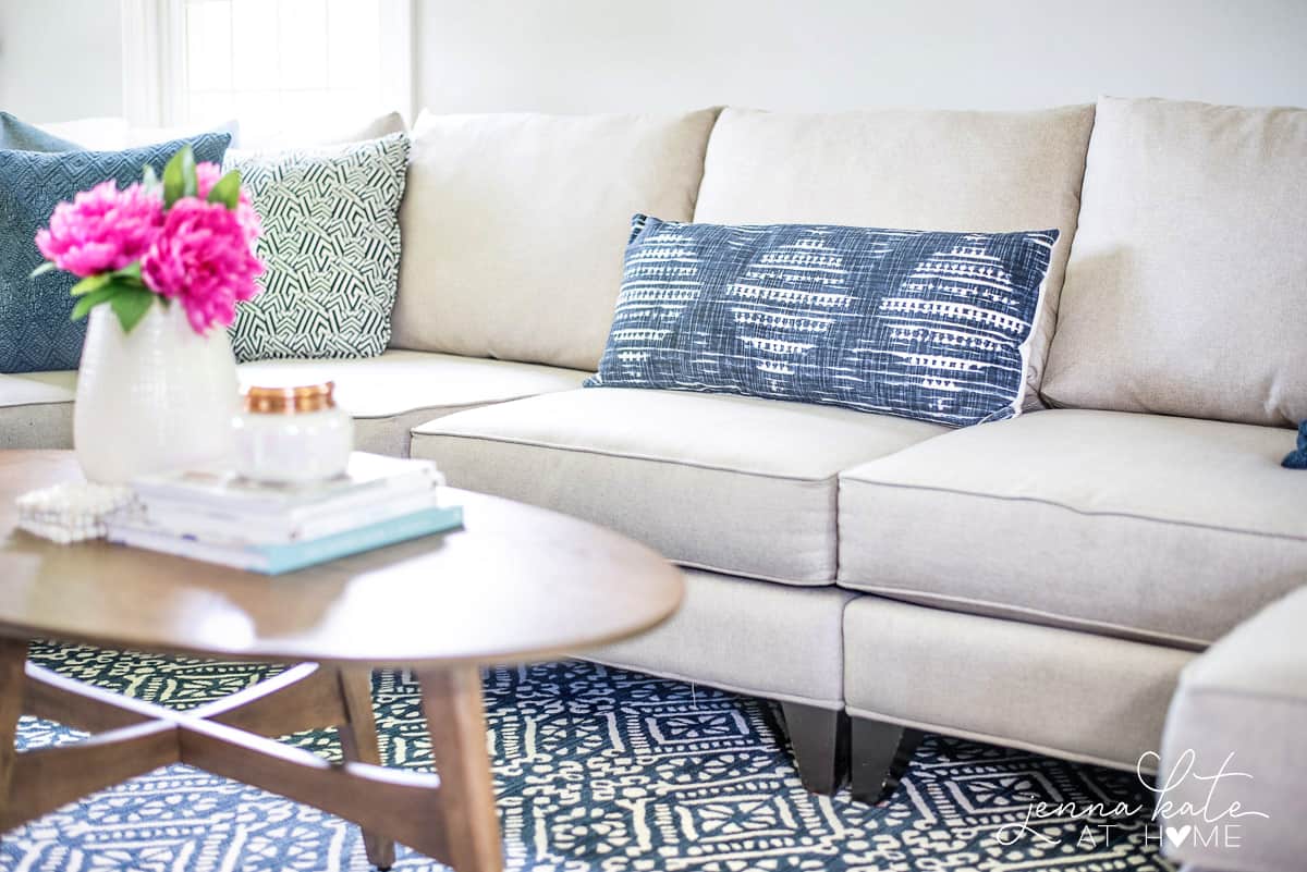 A light grey sofa in the living room with blue patterned pillows and a large blue & white rug