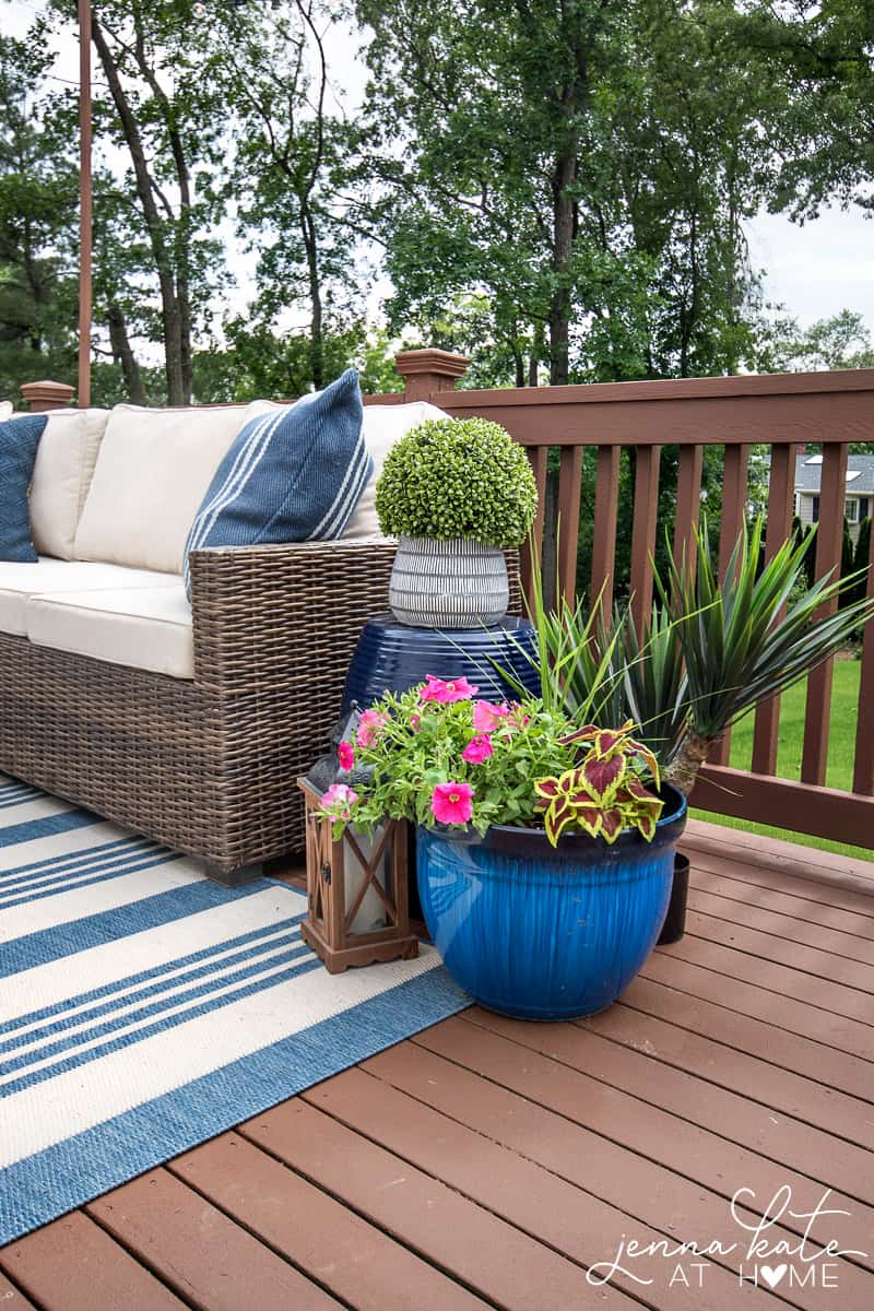 A collection of outdoor plants in various potters on a deck beside patio furniture