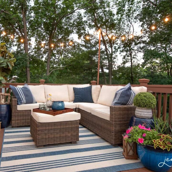 An outdoor wooden deck with blue and white furniture & decor, under a canopy of string lights