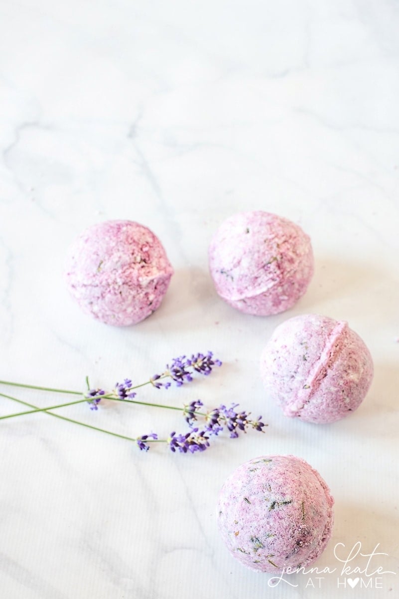 Four pink bath bombs infused with lavender flowers on a marble countertop