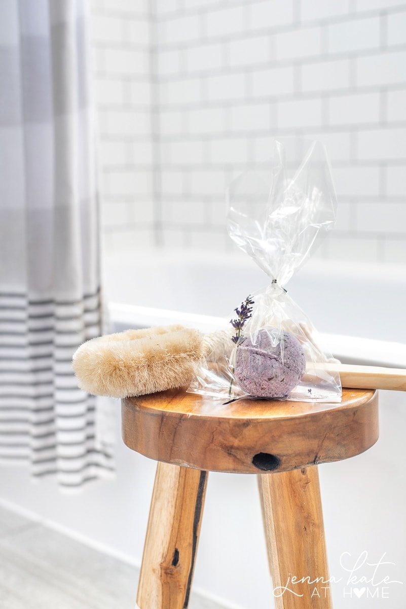 A purple bath bomb packaged as a gift in cellophane, on wooden stool near bath tub