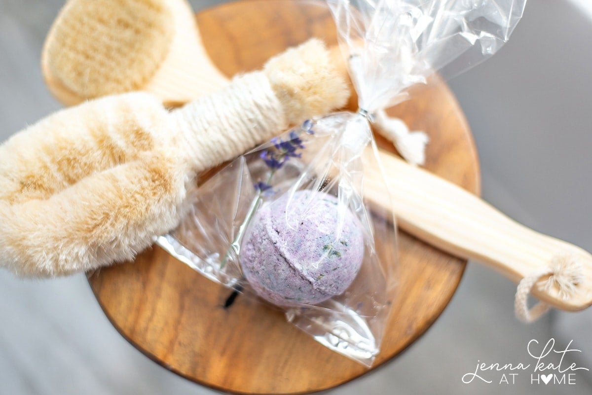 A purple bath bomb, resting on a wooden stool with other bath accessories