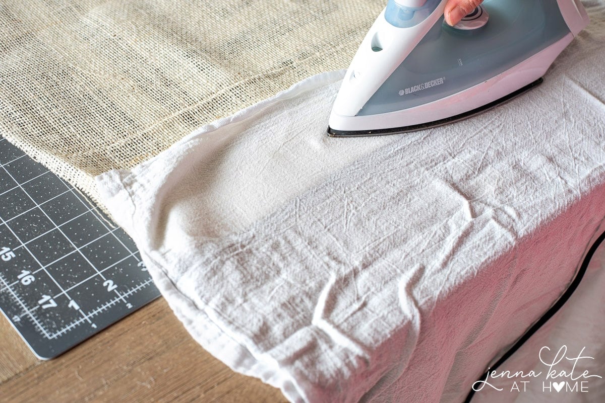 An iron is run over the burlap hem with a tea towel as a buffer, to secure the hem to the fusing tape.