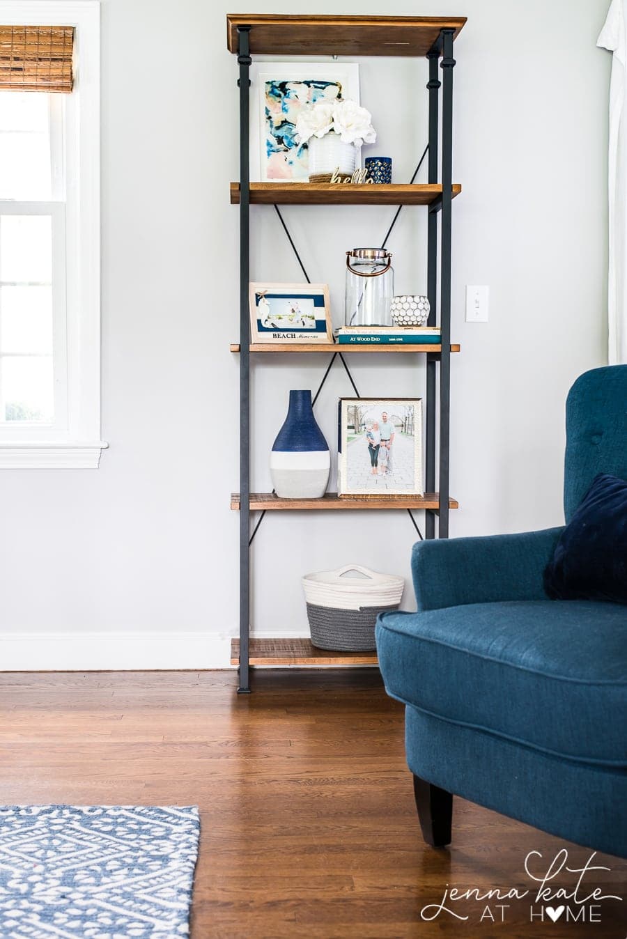 The edge of a tall, dark blue armchair, and an industrial -style wooden shelf in the distance, holding various decor items