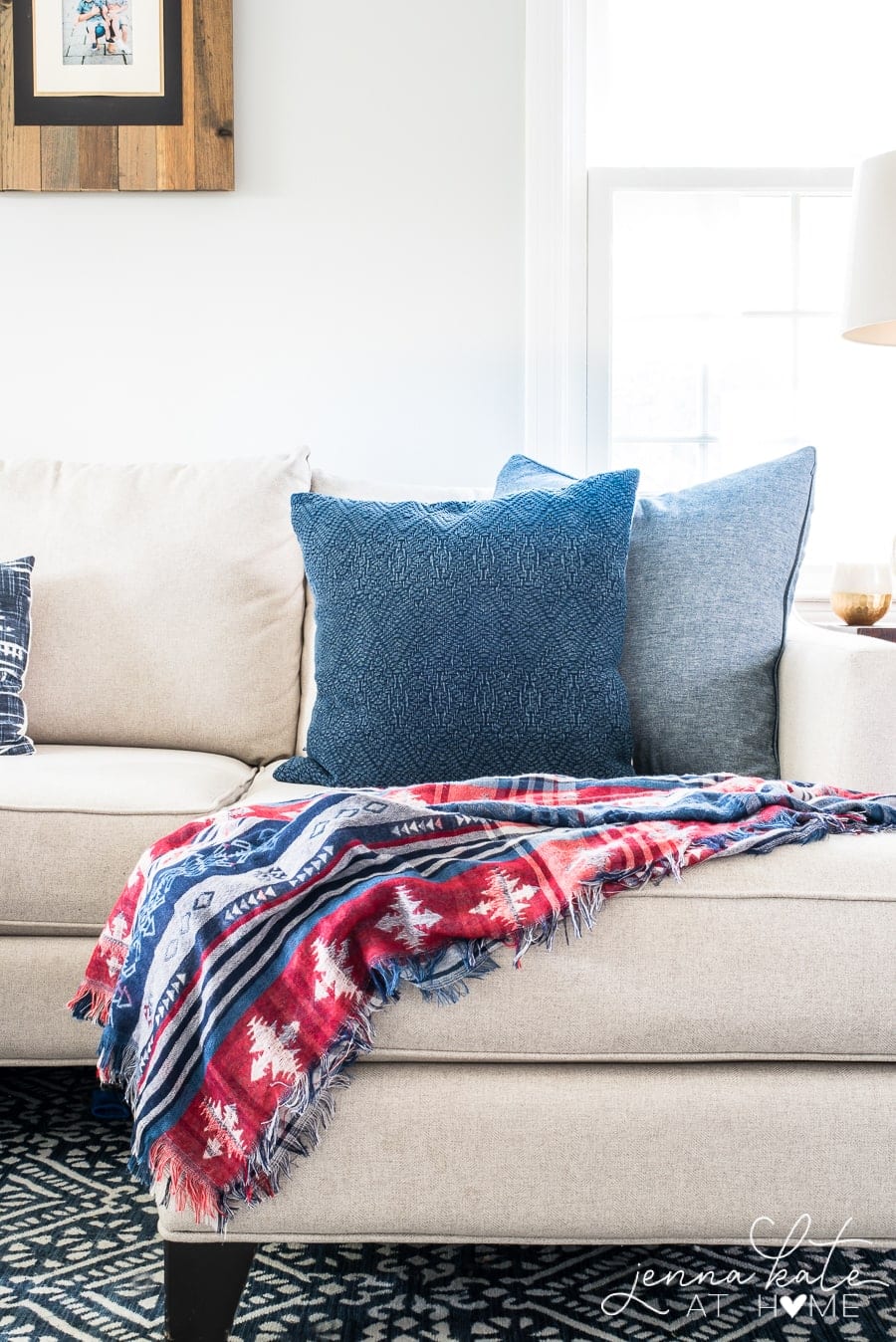 The end of a couch with a rustic blue and red throw and a pair of solid blue pillows