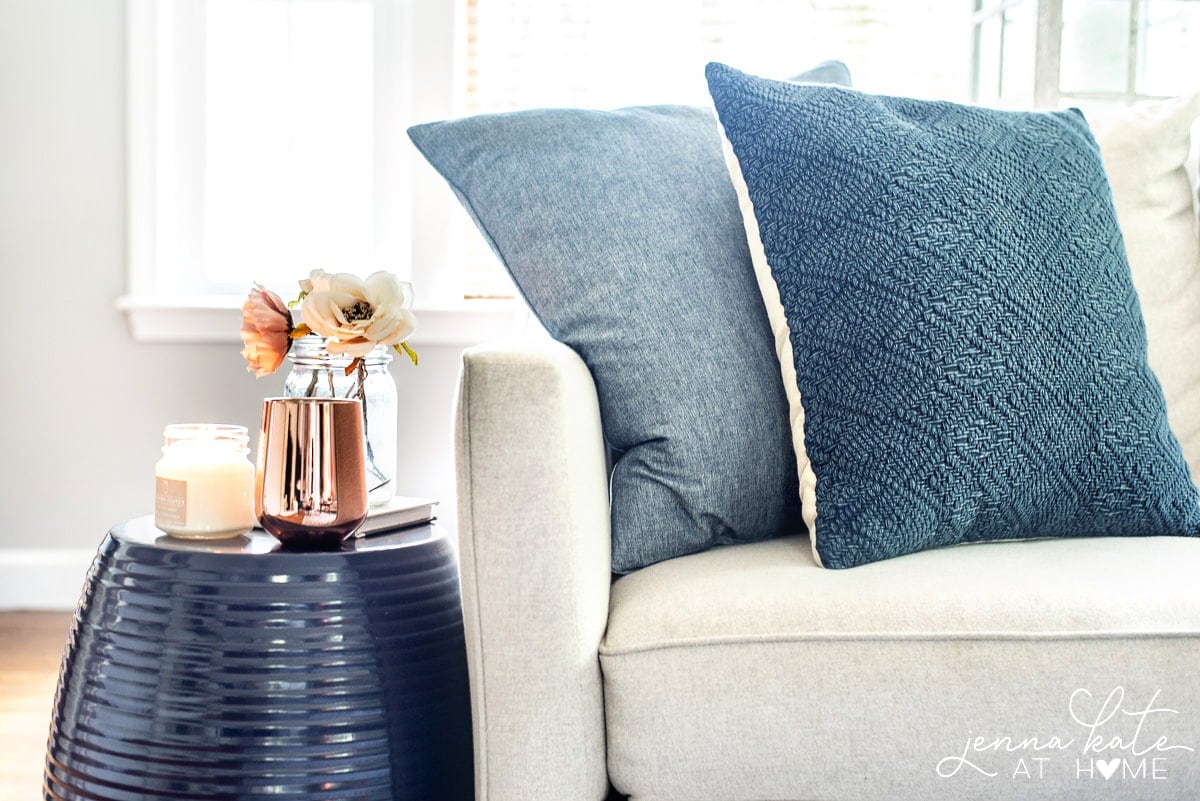 A cream couch with navy pillows and a side table beside it.