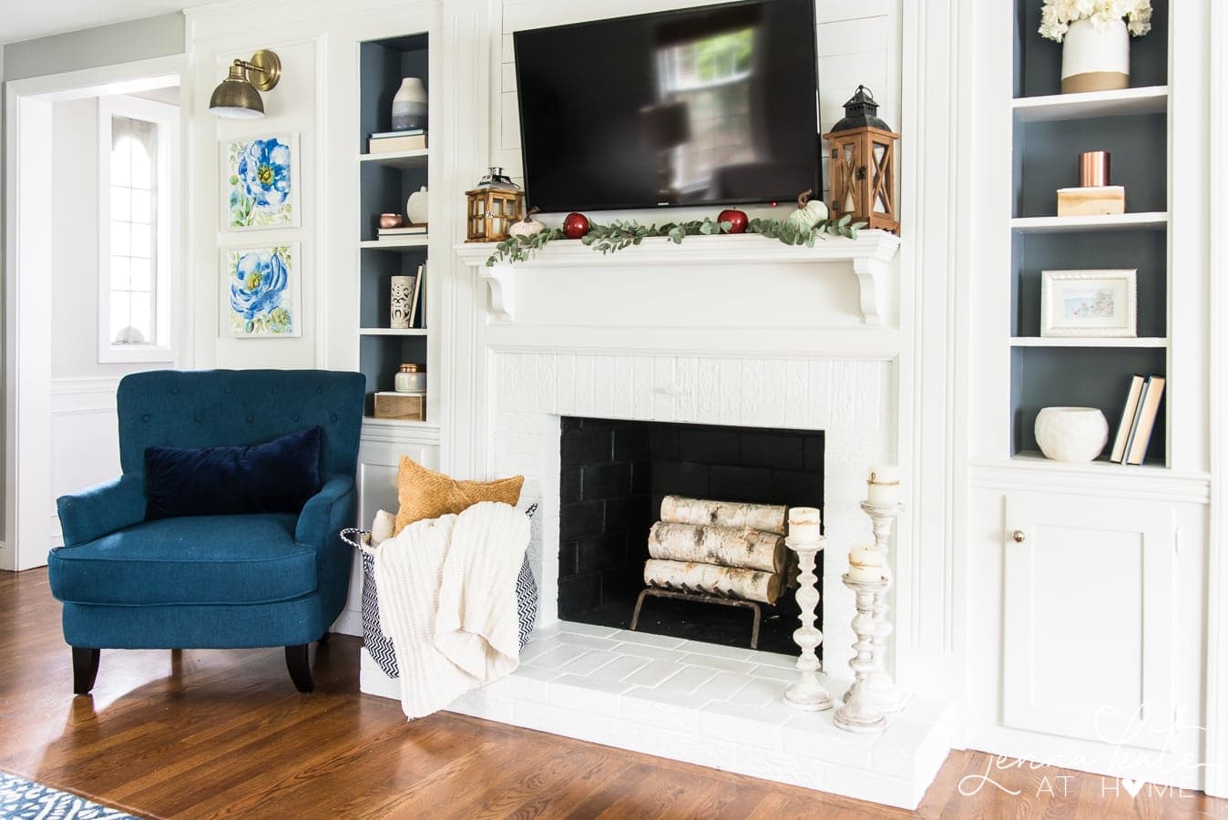 A fireplace with a wall-mounted television, fall decor on the mantel, and a blue armchair nearby
