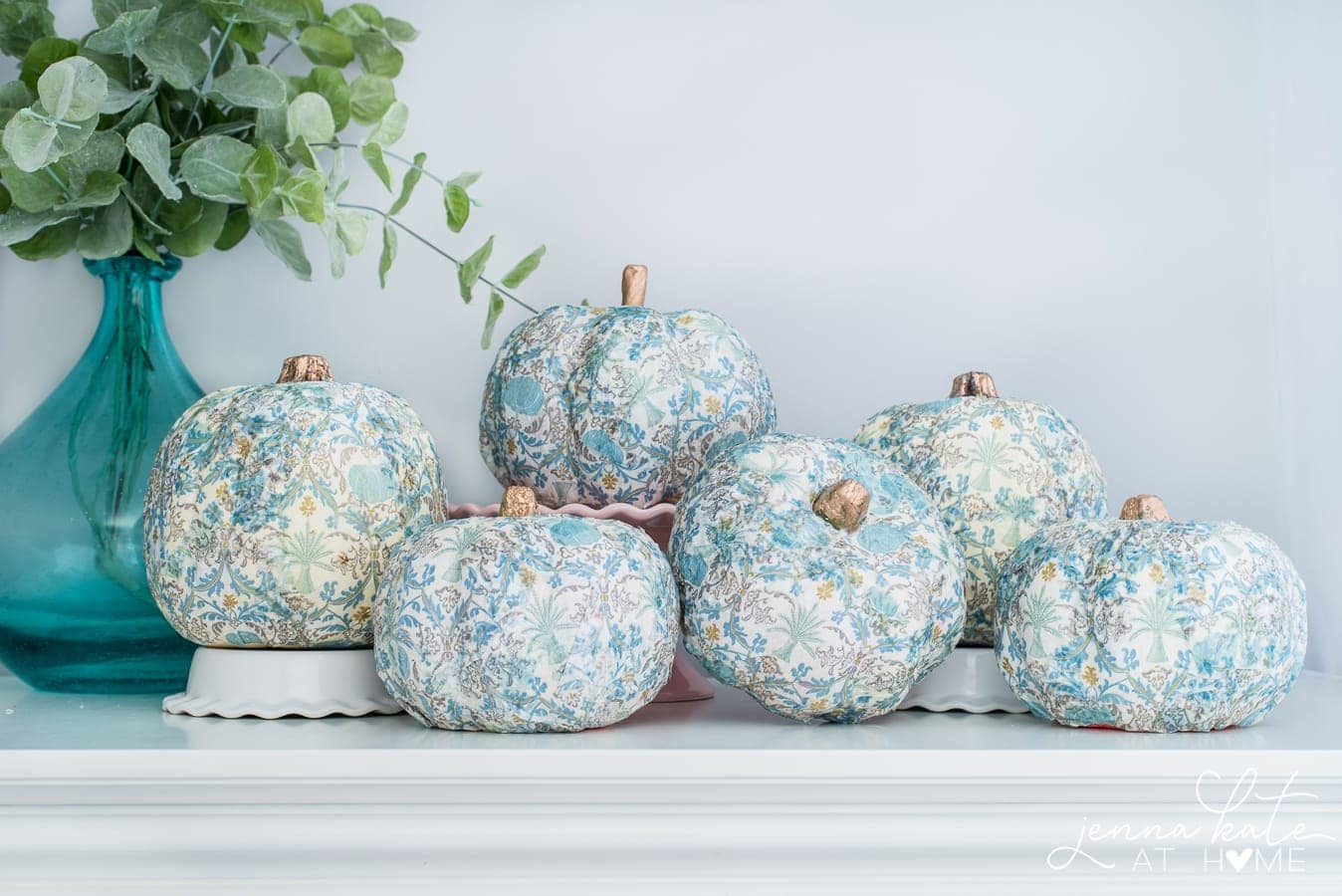 A collection of completed mod podge pumpkins resting on a table with a vase full of greenery.