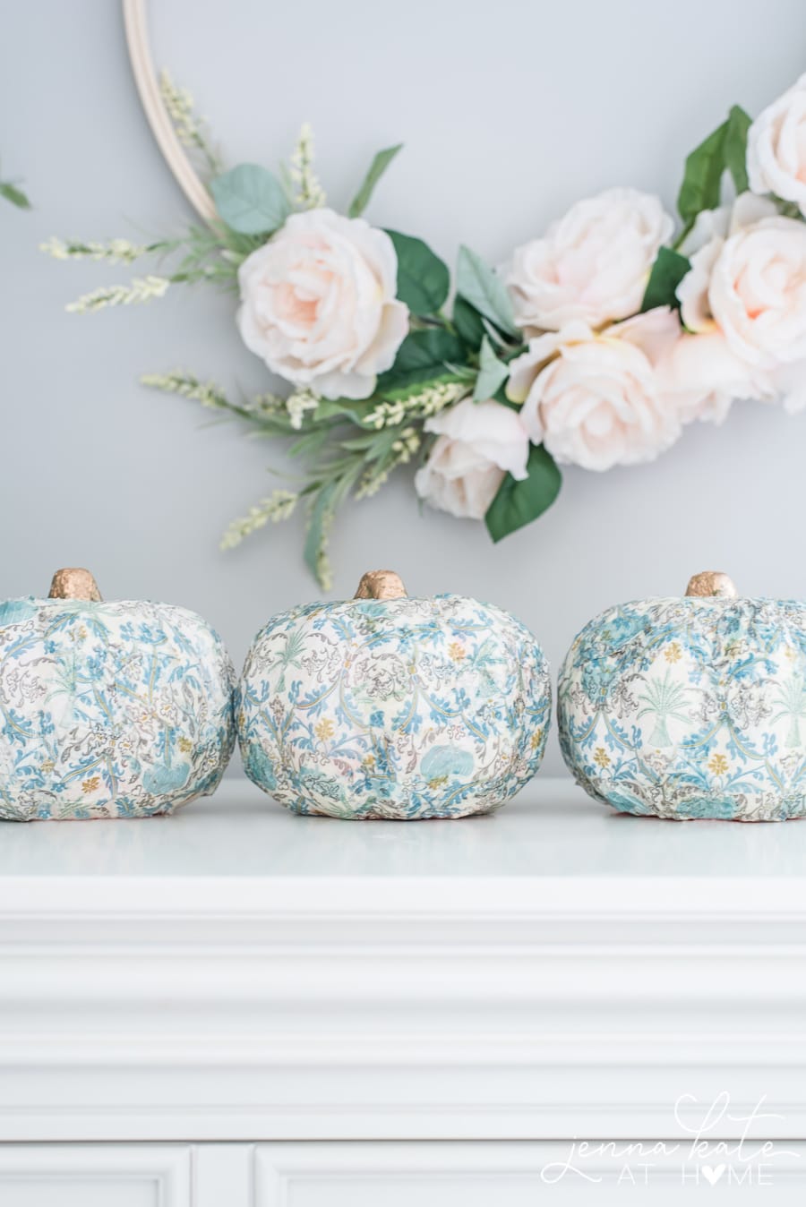 A photo of completed mod podge pumpkins sitting on a table with a floral wreath over top.