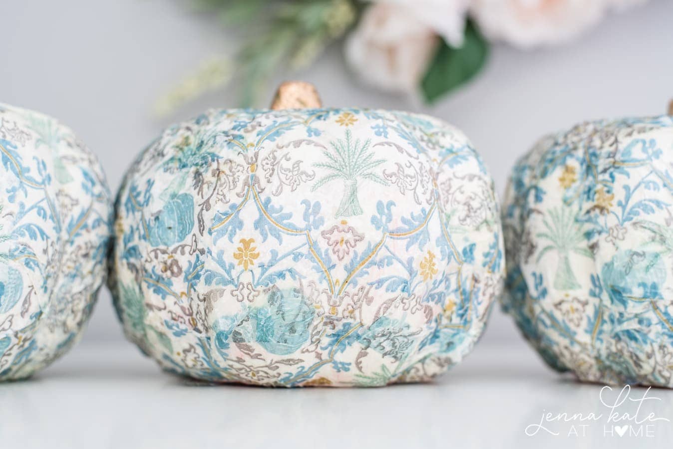 A close-up of a pumpkin after it has been covered in a vintage patterned napkin and the tip has been painted gold.