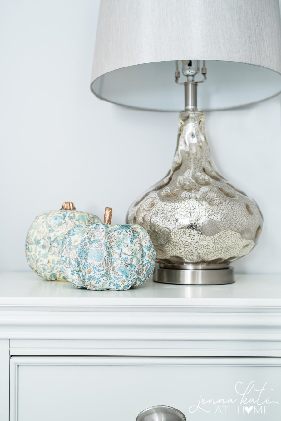 Two mod podge pumpkins displayed beside a large lamp on a console.