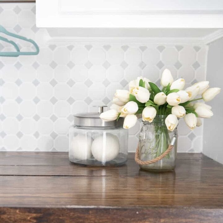 Bouquet of white flowers and glass jar rest on wooden countertop in laundry room
