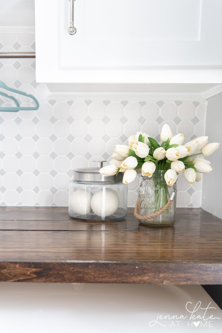 Bouquet of white flowers and glass jar rest on wooden countertop in laundry room