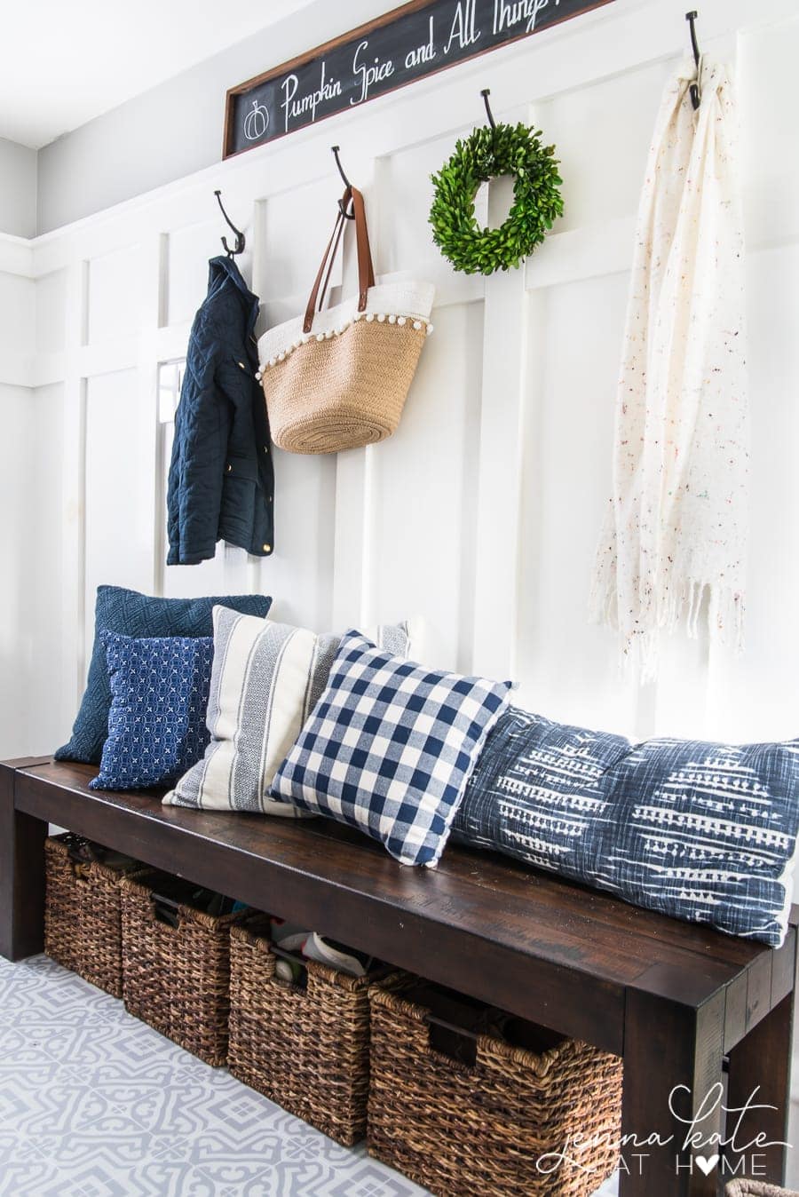 A dark wood bench with large, wicker baskets below, and an assortment of patterned, blue pillows on top