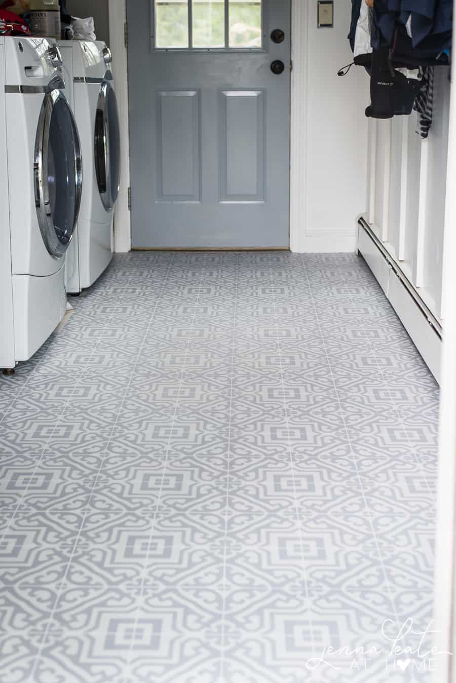 A lower shot of the room, focusing on the newly-installed grey patterned vinyl flooring, with the washer & dryer on the right and a door to the outside straight ahead.