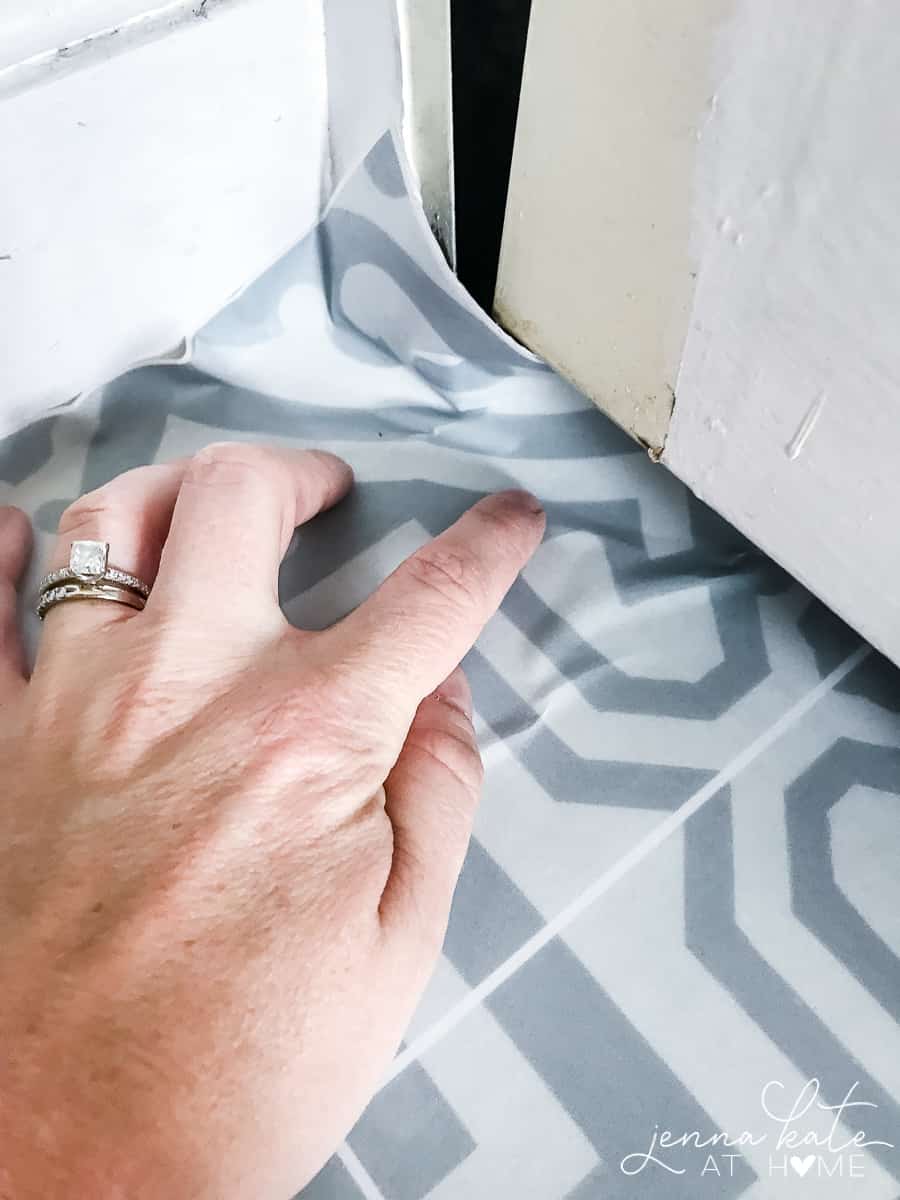 Jenna in the process of carefully inserting the blue/grey vinyl floor cover underneath a cabinet