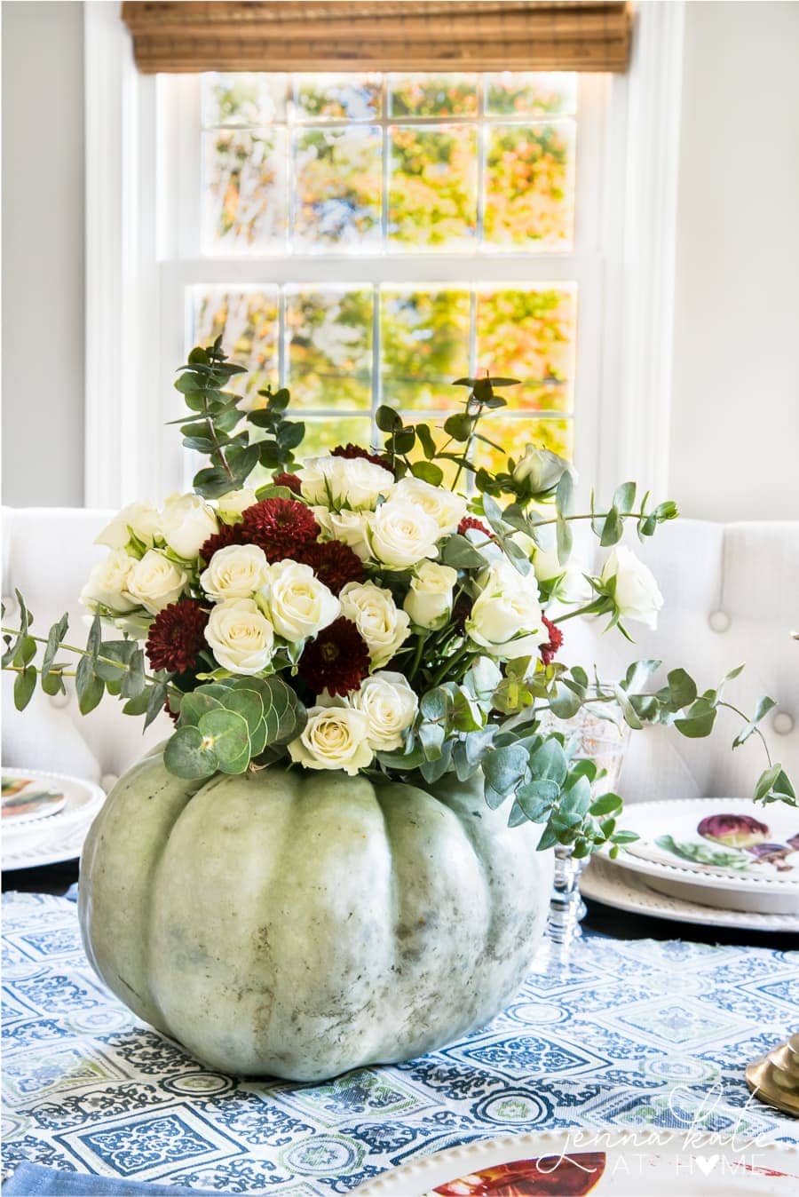 A large, light green pumpkin holding an assortment of white and dark red flowers and sprigs of eucalyptus. 