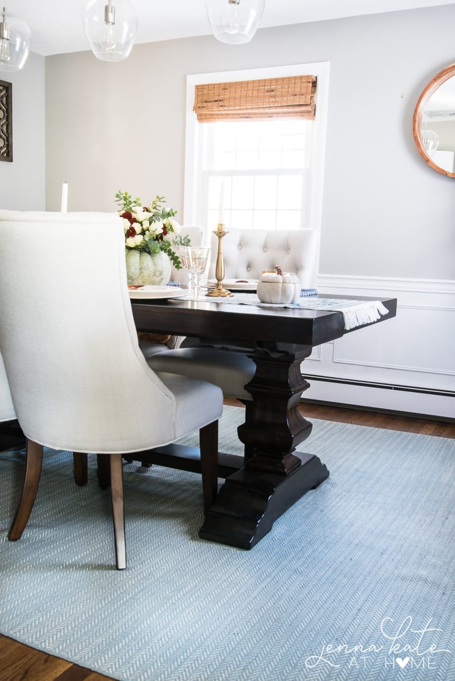 A distant view of the dining table with the back of an upholstered chair, showing the light blue rug below the dining table