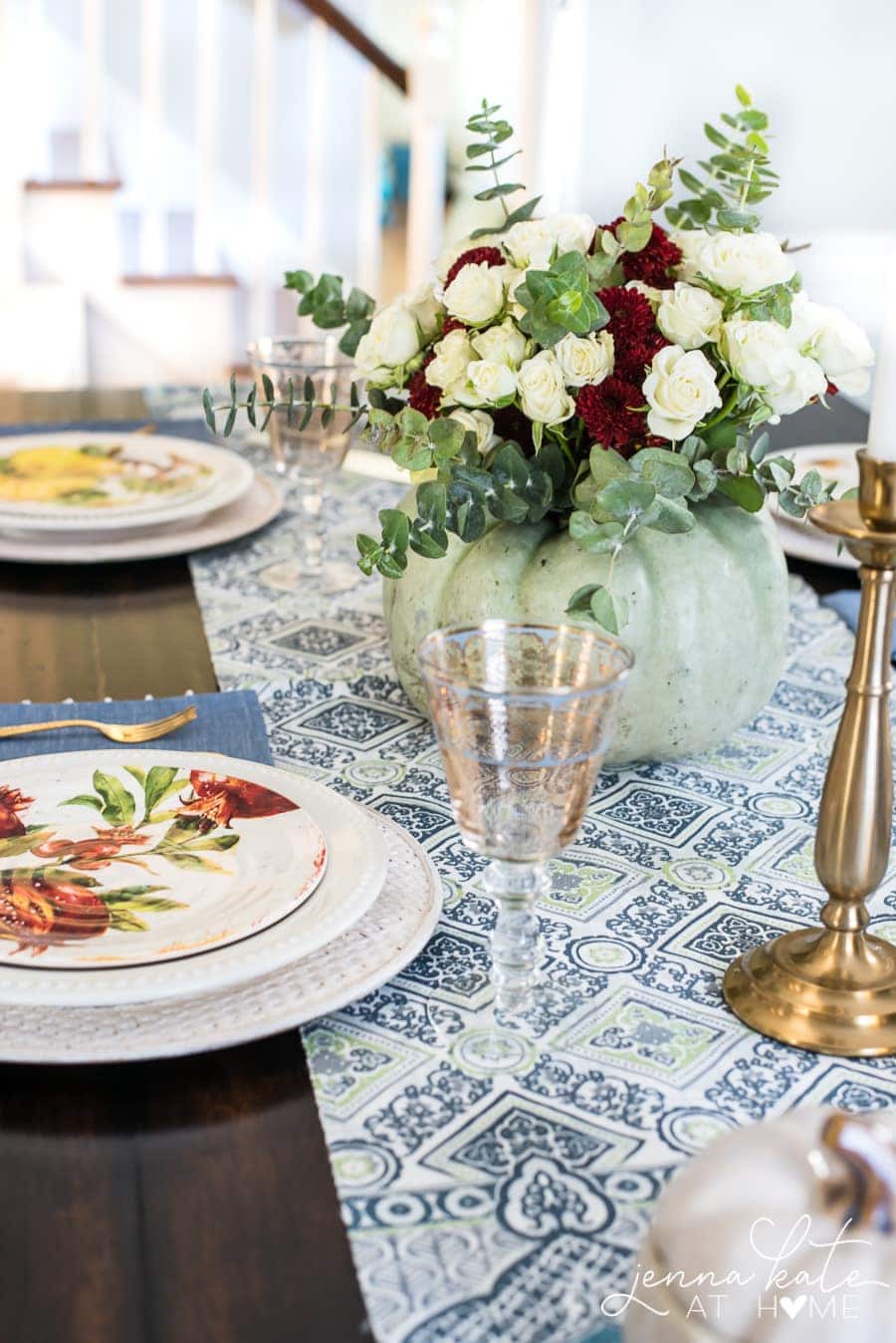 A close-up of the blue and white table runner, golden candlestick, blue and gold patterned stemware and fall-themed plates