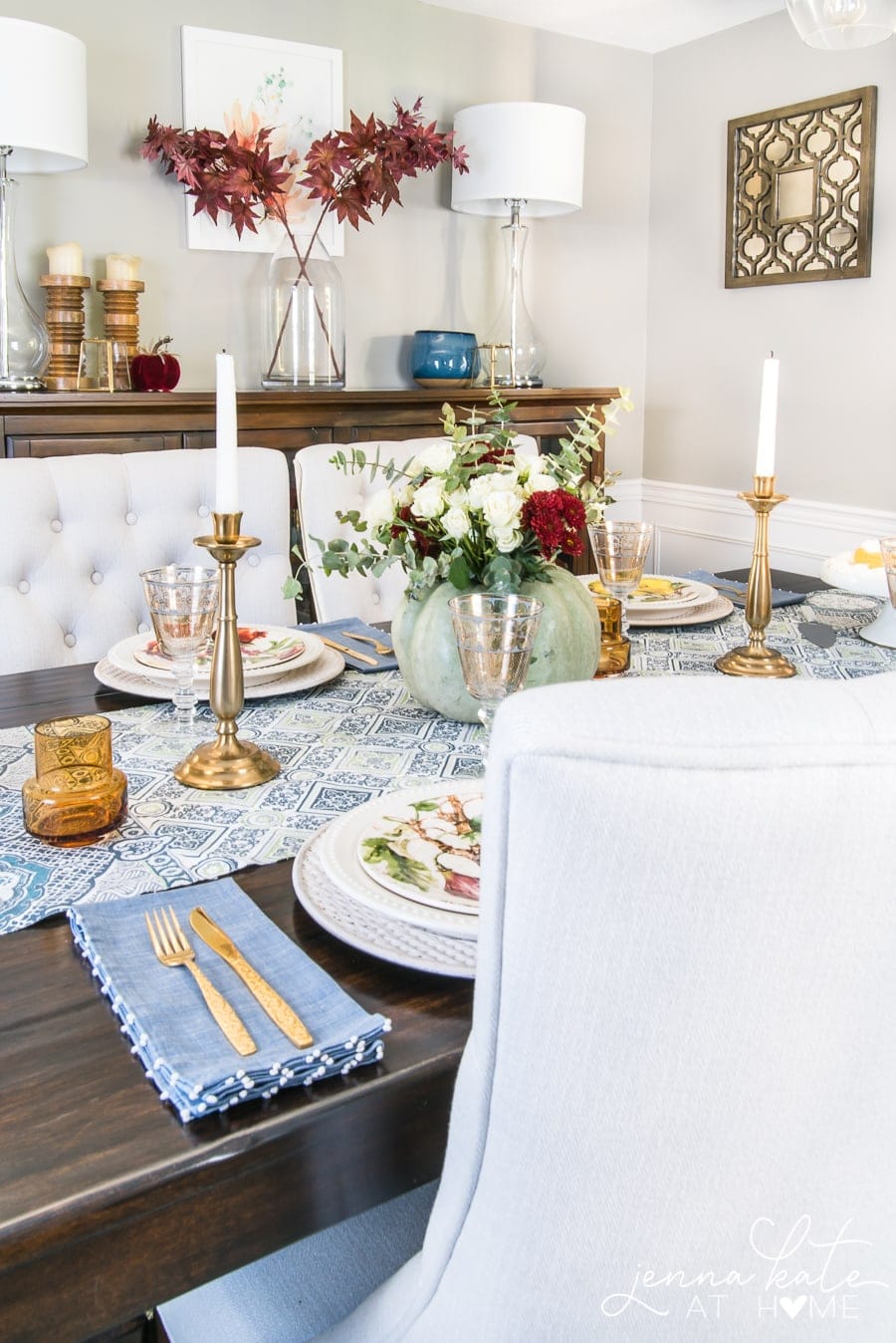 A different view of the dining table, showing the gold utensils resting on light blue cloth napkins, near brown glasses and gold candlesticks