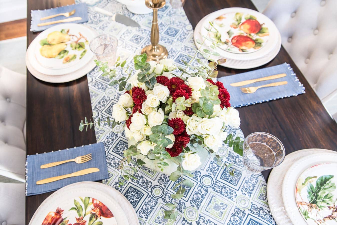 A top view of the dining table, showing the tips of the floral centerpiece, and the place settings, including the gold utensils