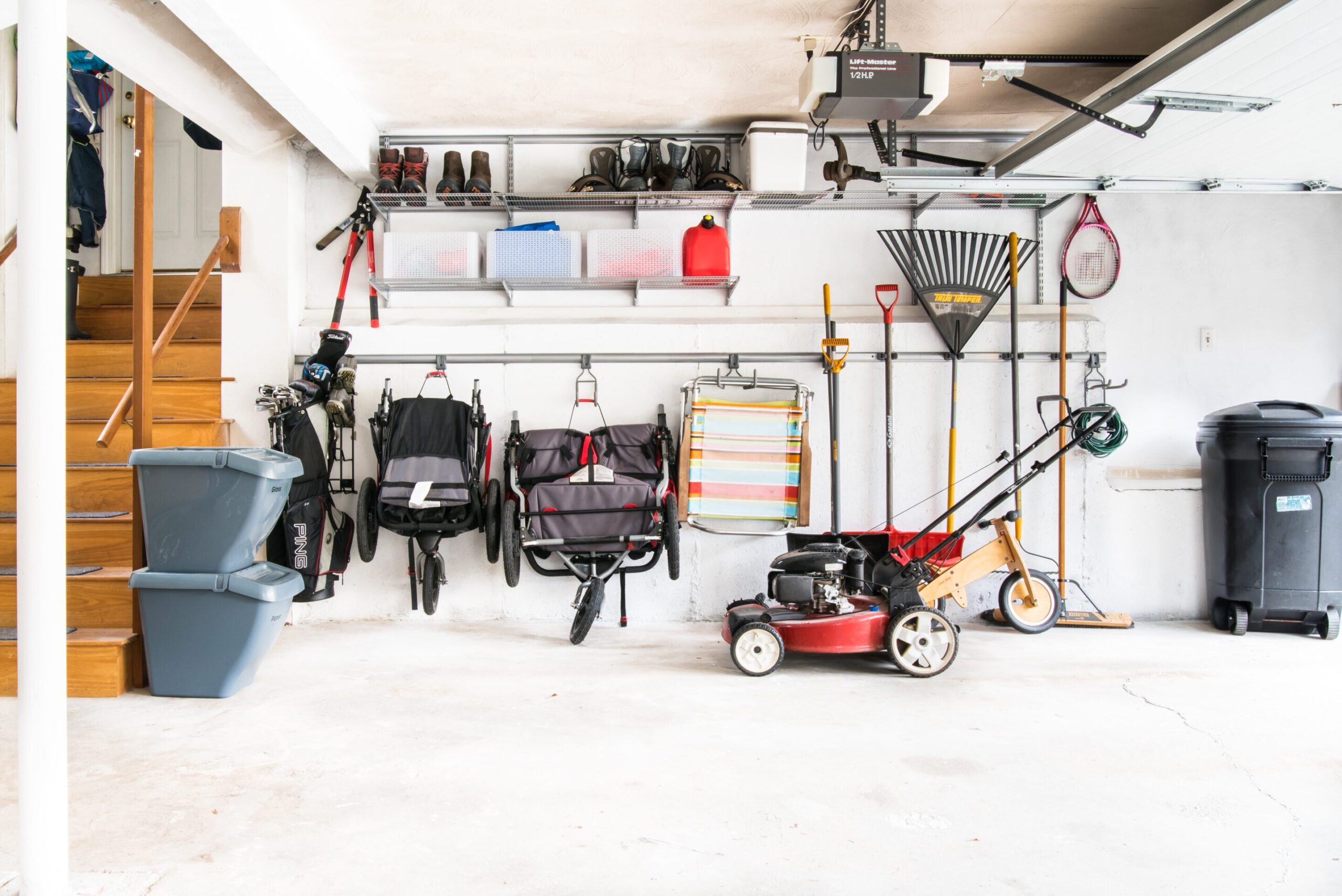 One wall of a garage, with built-in shelves and racks to hold various garden tools, strollers, boots, etc.