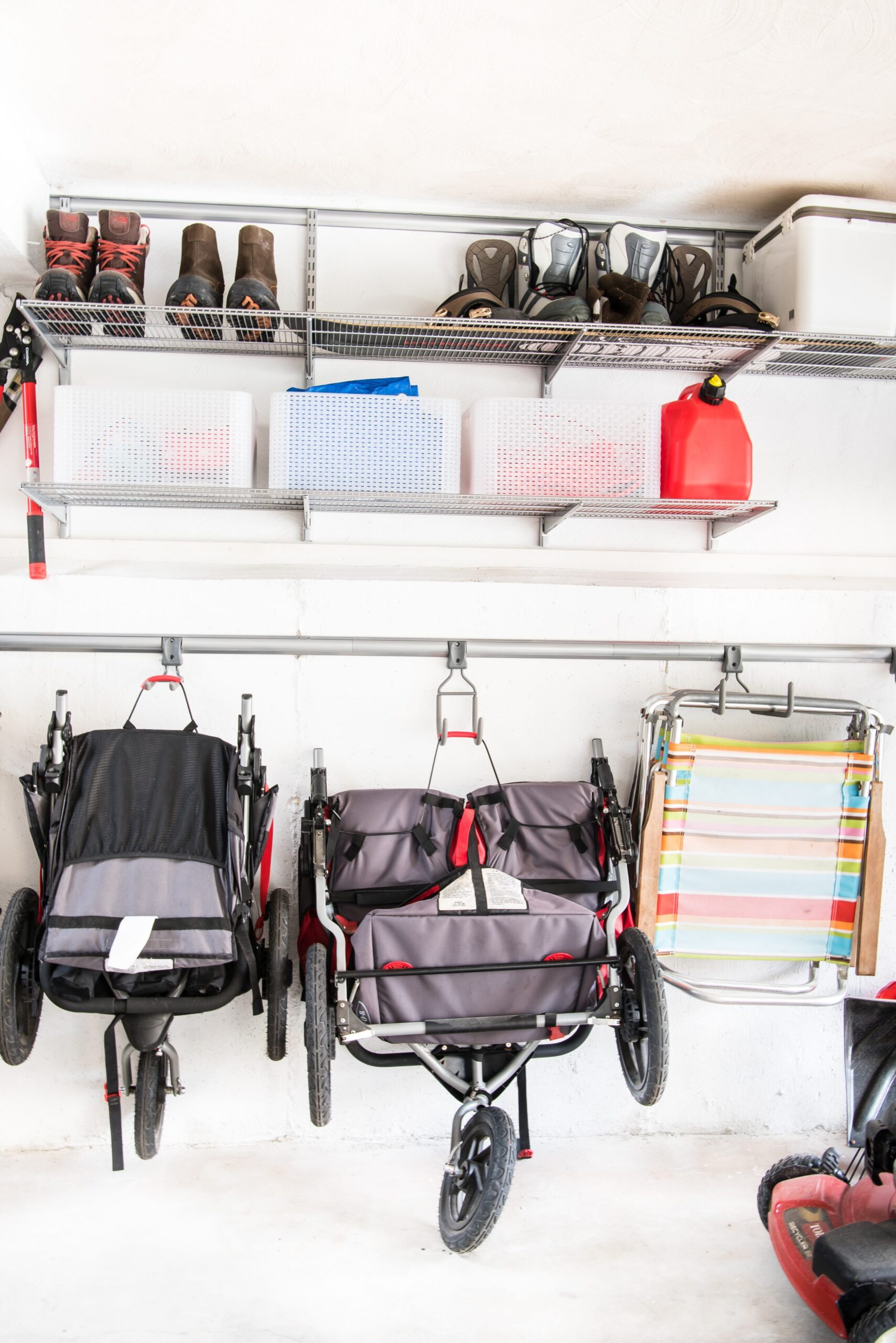 Strollers, Beach chairs, and other objects hanging from wall hooks on a garage wall.