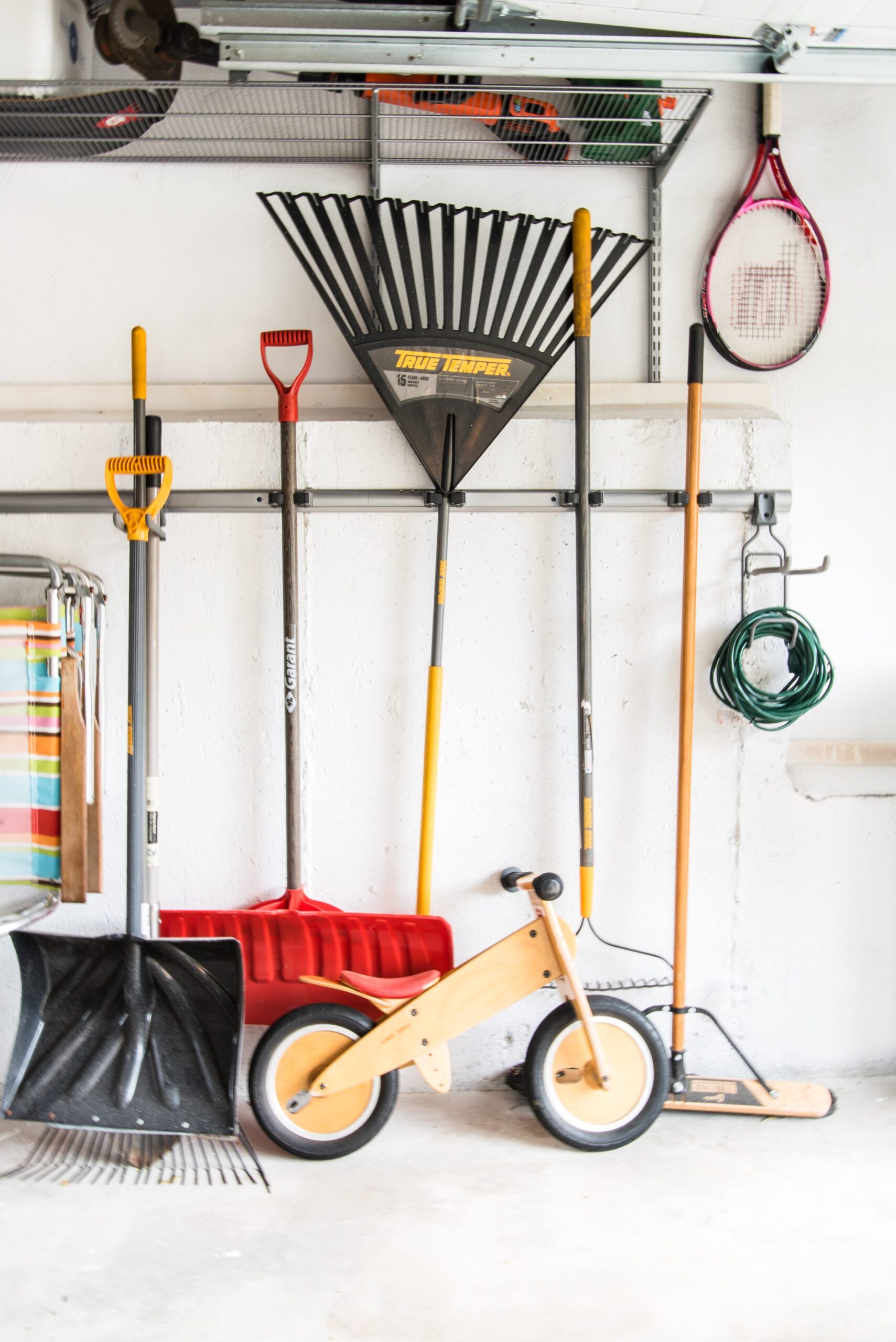 Rakes, Shovels, and other outdoor equipment attached to wall hooks on a garage wall.