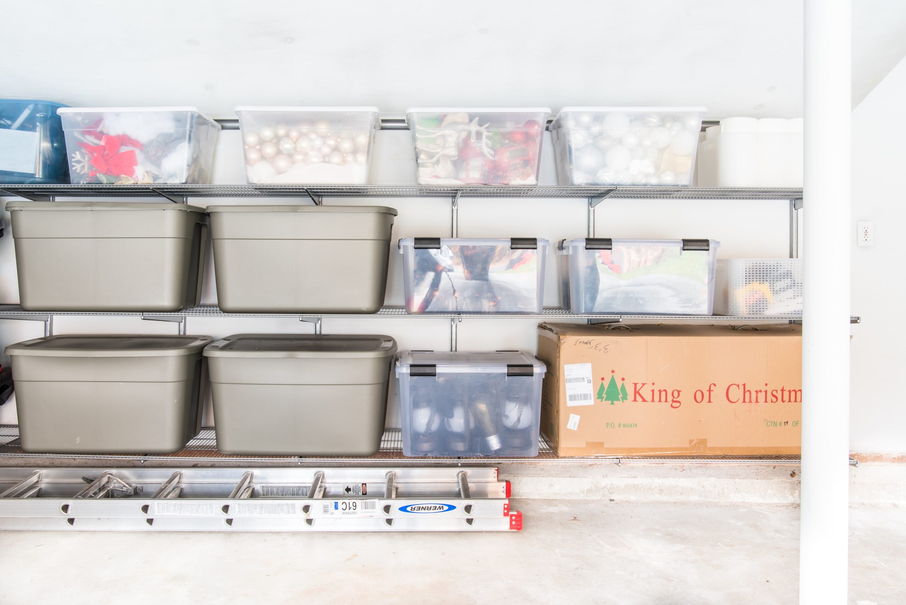 Garage shelves with clear tote bins full of colored Christmas ornaments 