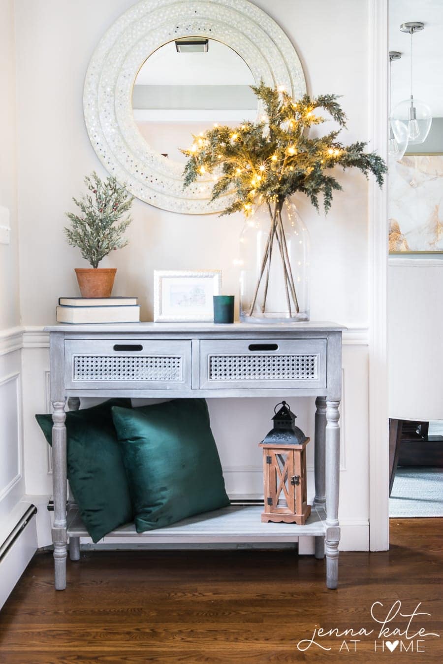 console table in entryway with mirror above it and vase of lit evergeen stems