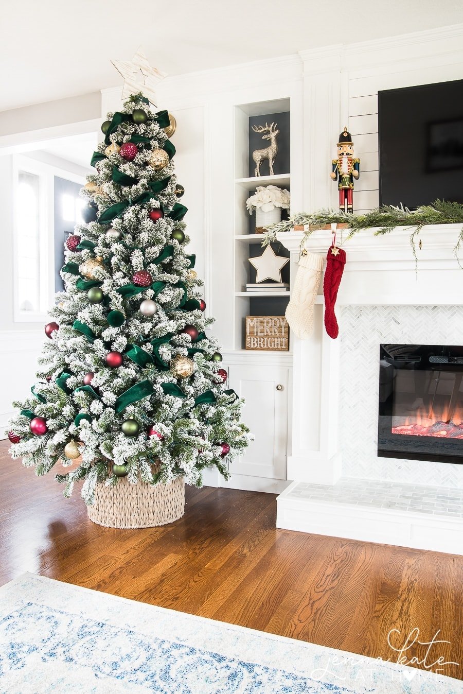 A Christmas tree in a basket sitting next to a mantel with stockings hung.