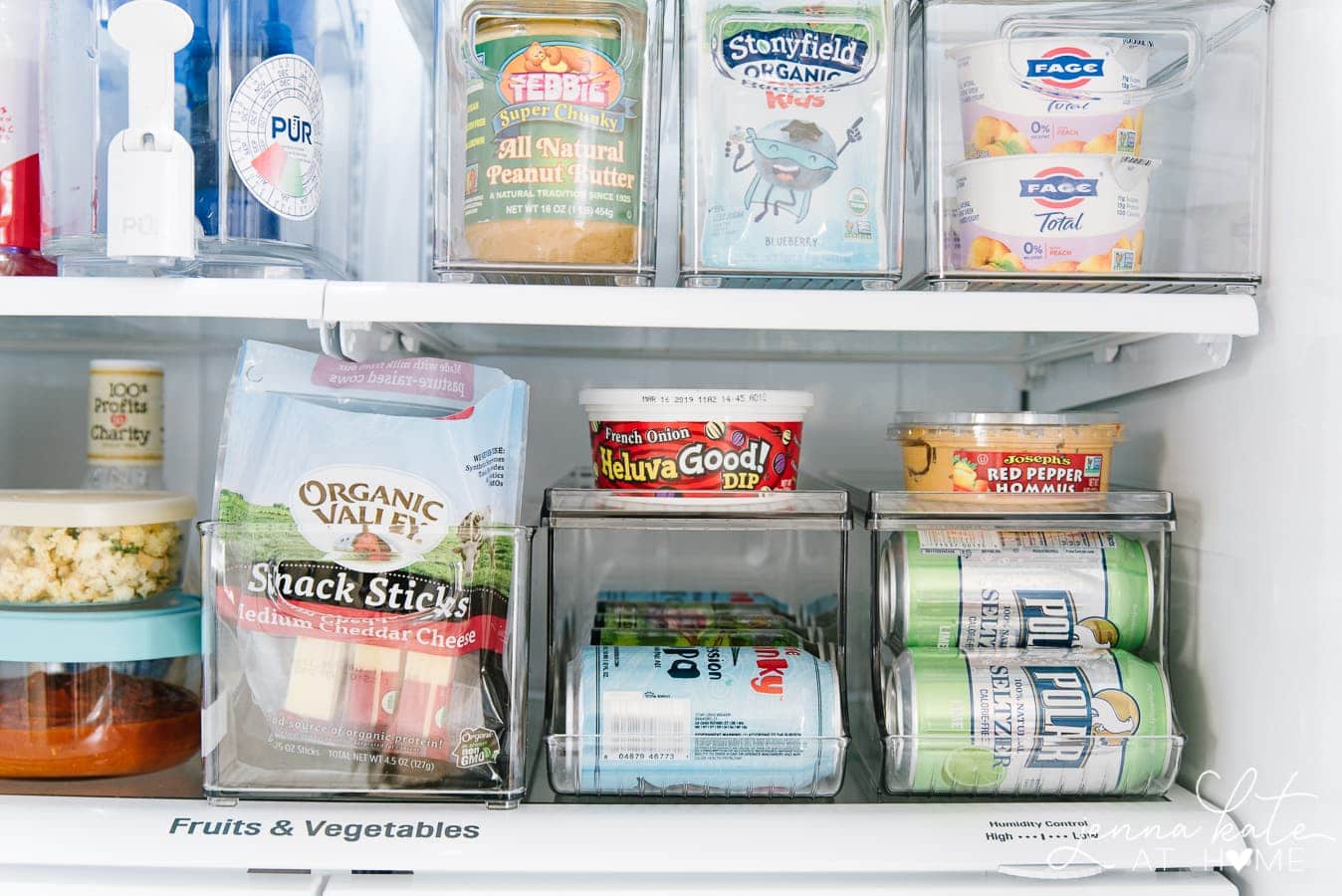 An open refrigerator with plastic organizers to hold cans of beverages, cheese snacks, yogurt and bottles of water