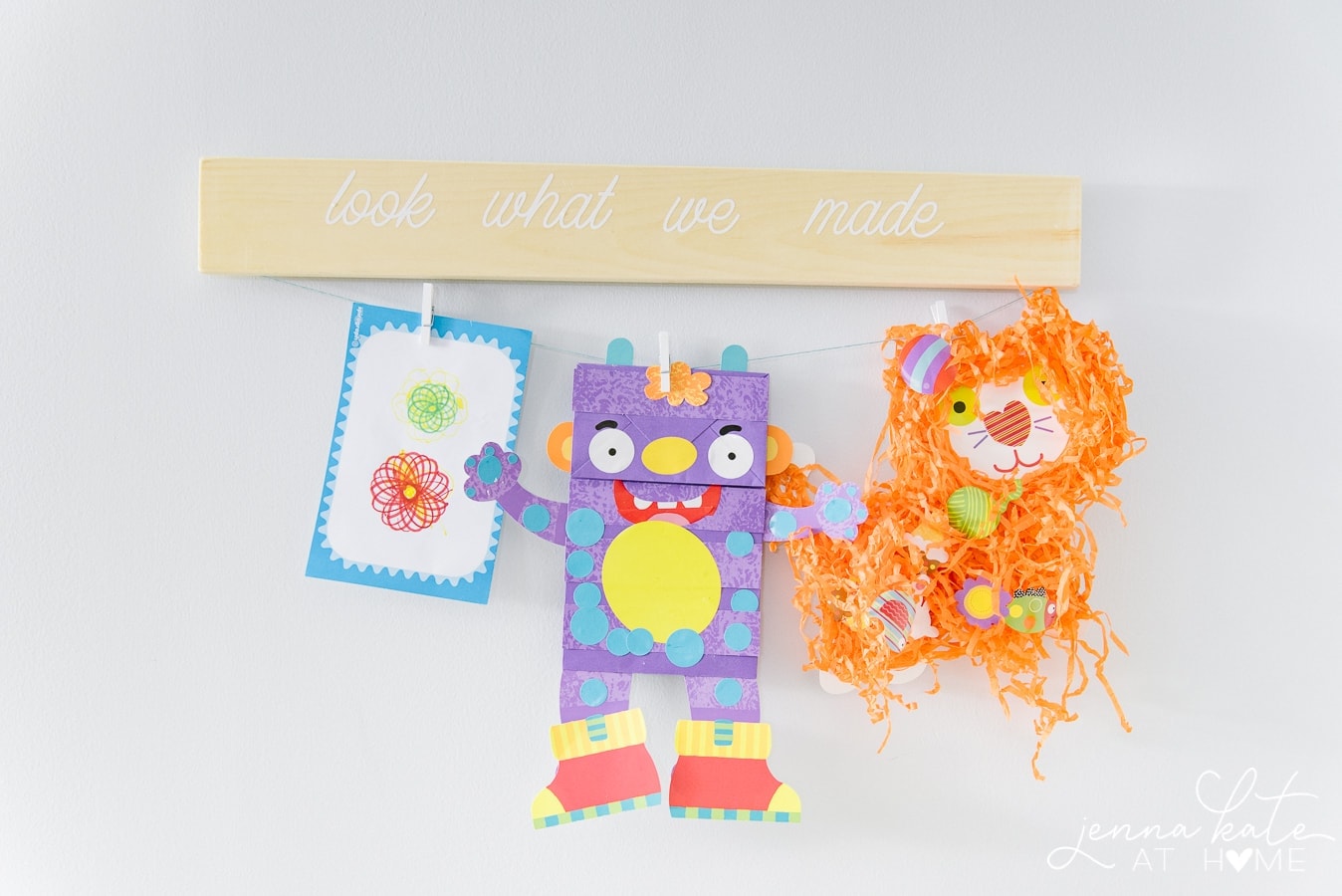 A wooden artwork hanger with the words \"Look what we made\", and a clothes line and pegs holding colorful artwork