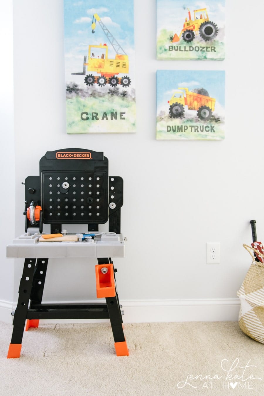 A trio paintings of construction vehicles on the wall, with a toy work bench nearby