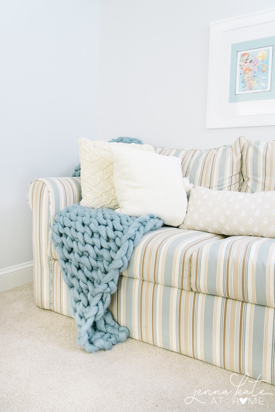 A beige and blue striped sofa, with beige throw pillows and a thick blue blanket