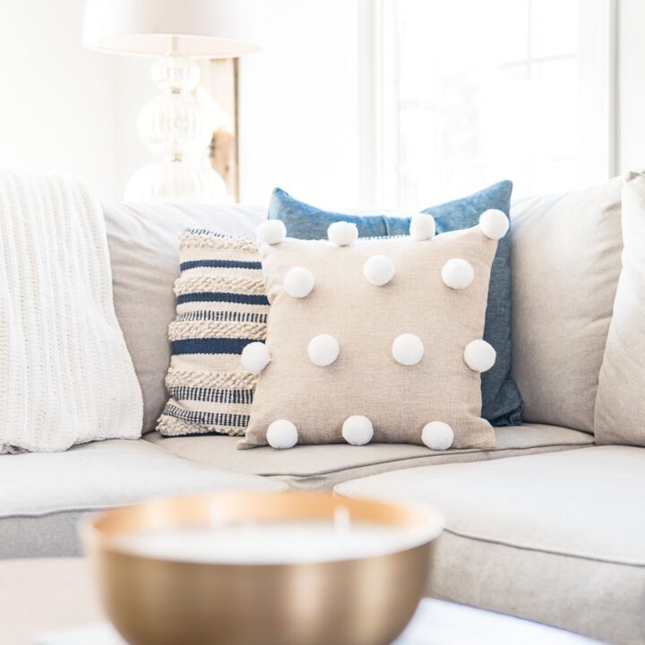 A close up of three pillows on a living room sectional with the pom pom pillow at the front